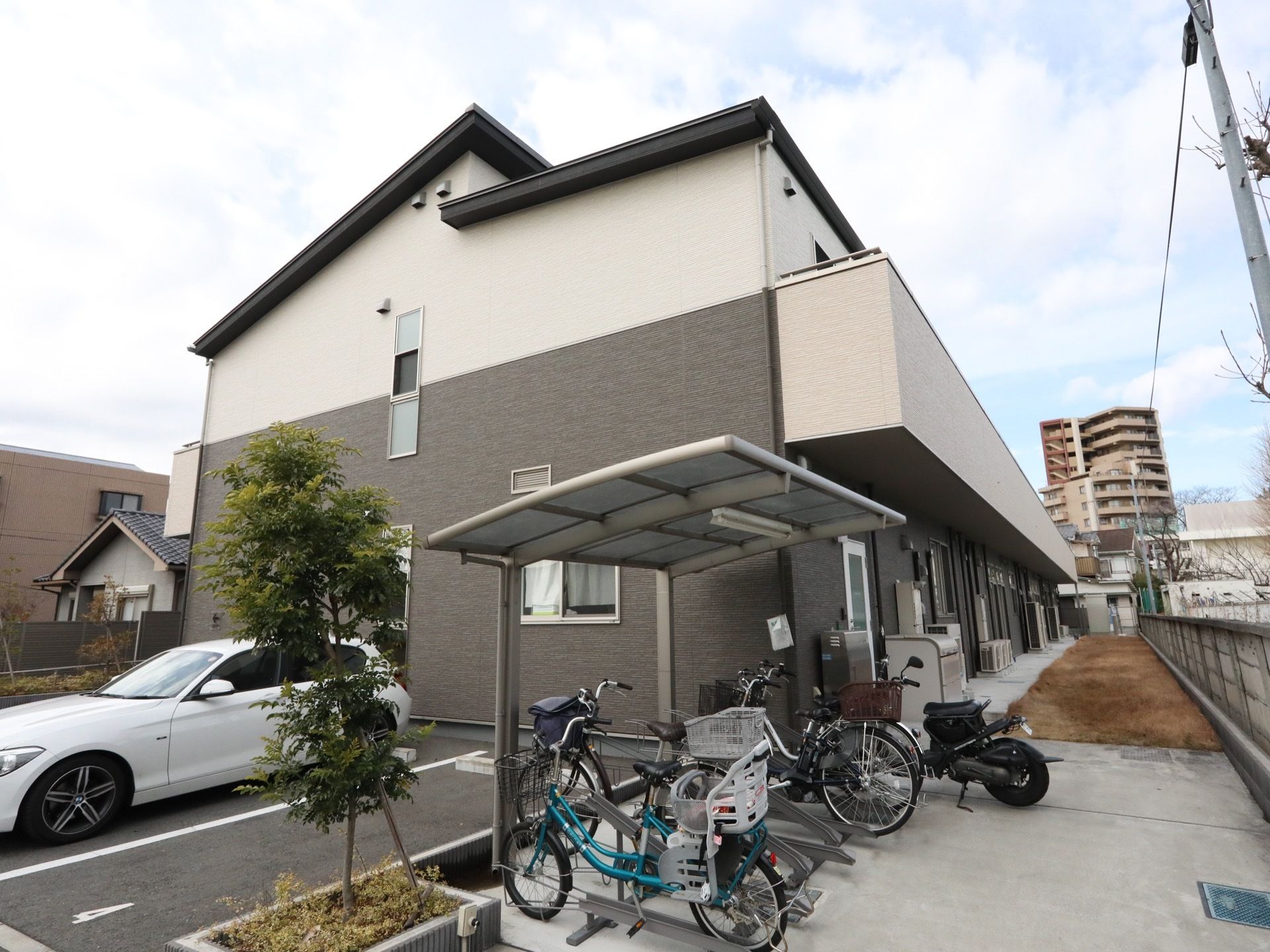 ２階建ての集合住宅が建っている。建物の手前には、駐車スペースと、屋根の付いた駐輪場が設けられている。