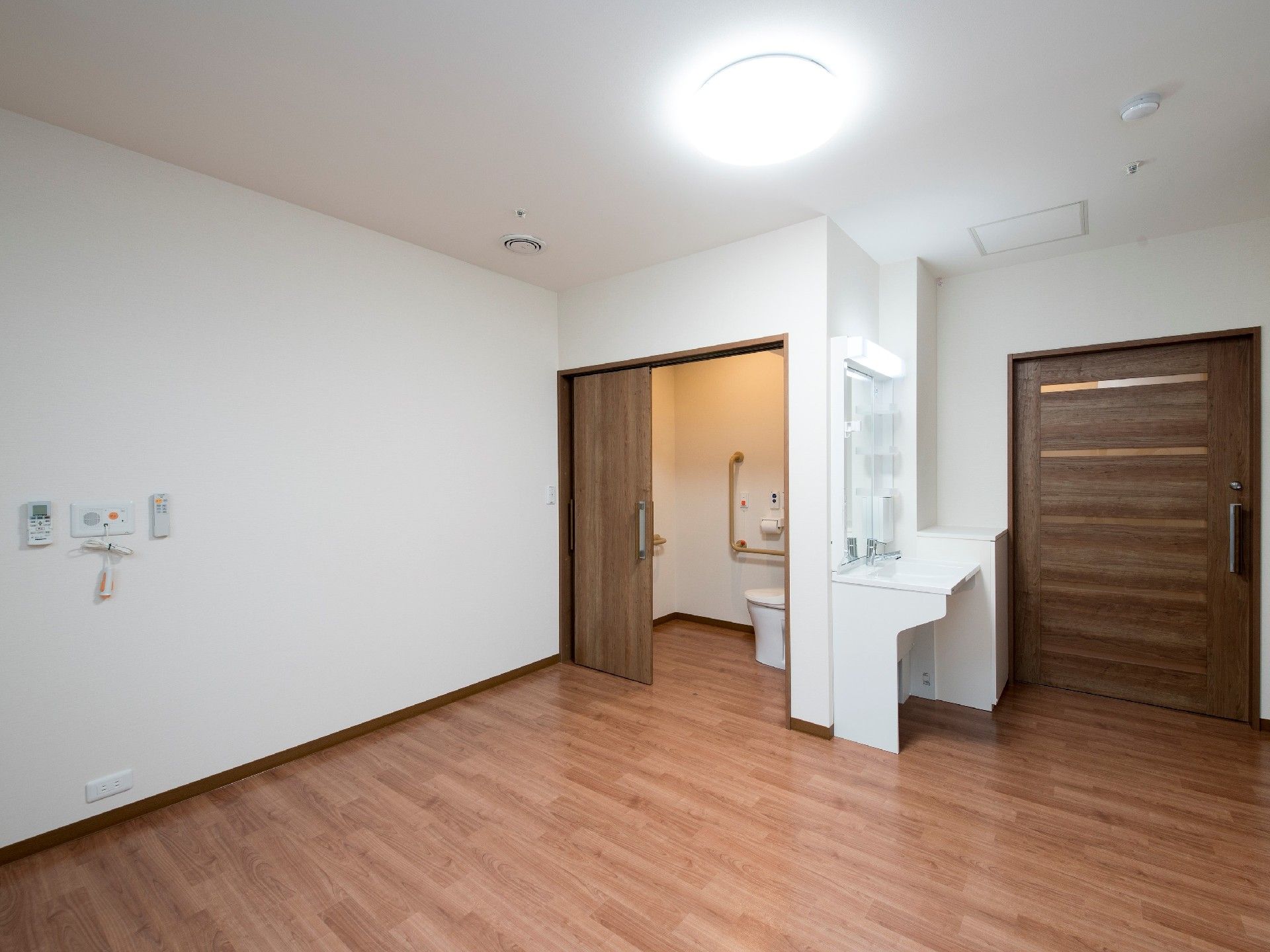緊急通報装置が壁につき、トイレも設置されている居室はフローリングで車いす対応の洗面所もある。