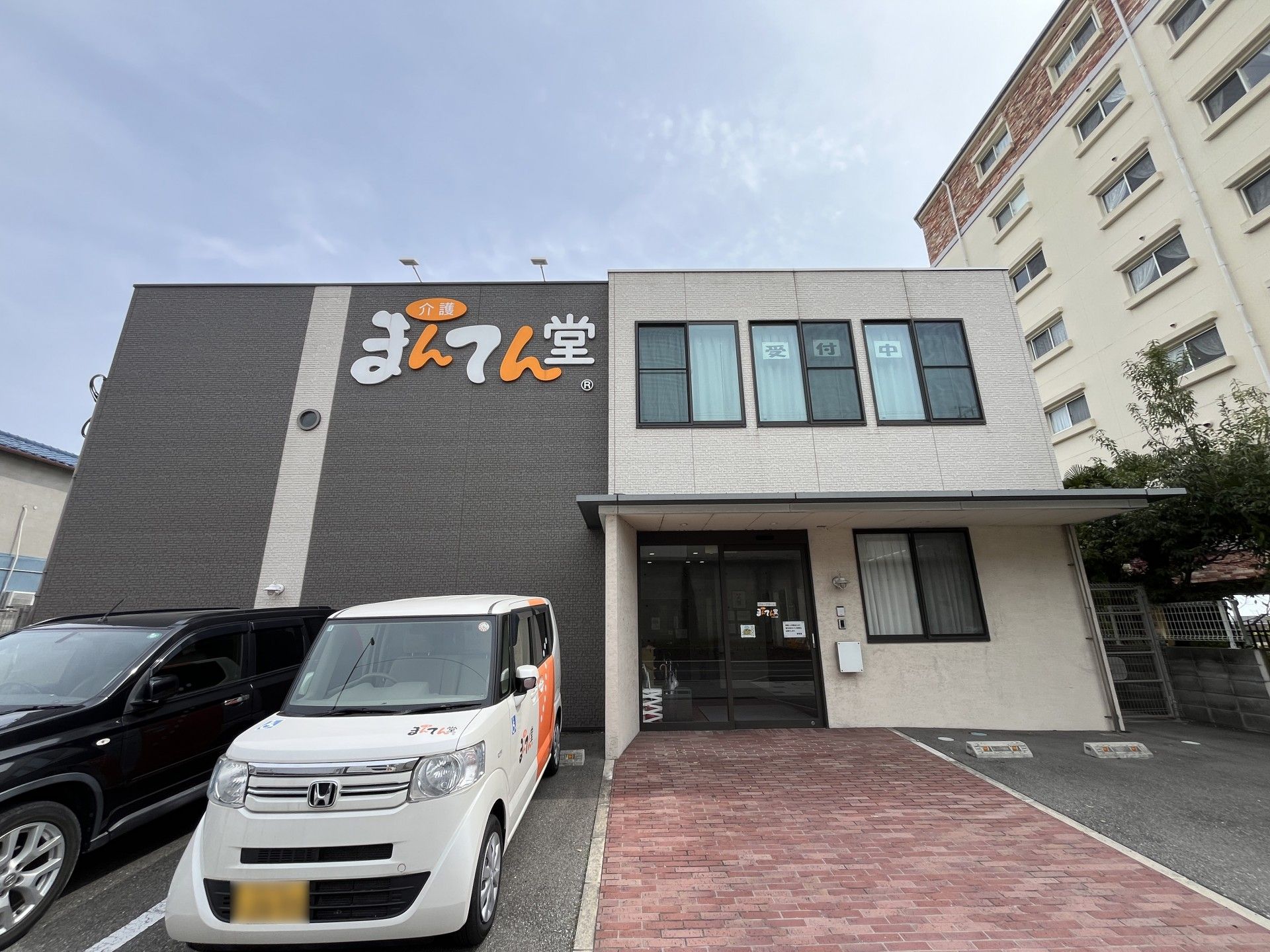 ホーム名が書かれた外壁が印象的な2階建ての建物。周辺には木が植えられ、のぼりも立っている。