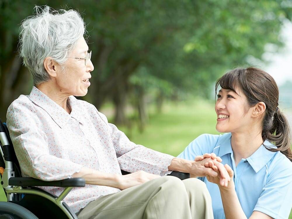 車椅子に乗った高齢女性と向き合う女性ヘルパー