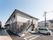 白とグレーの2階建て他の建物。玄関先には屋根があり、広い駐輪場もある。