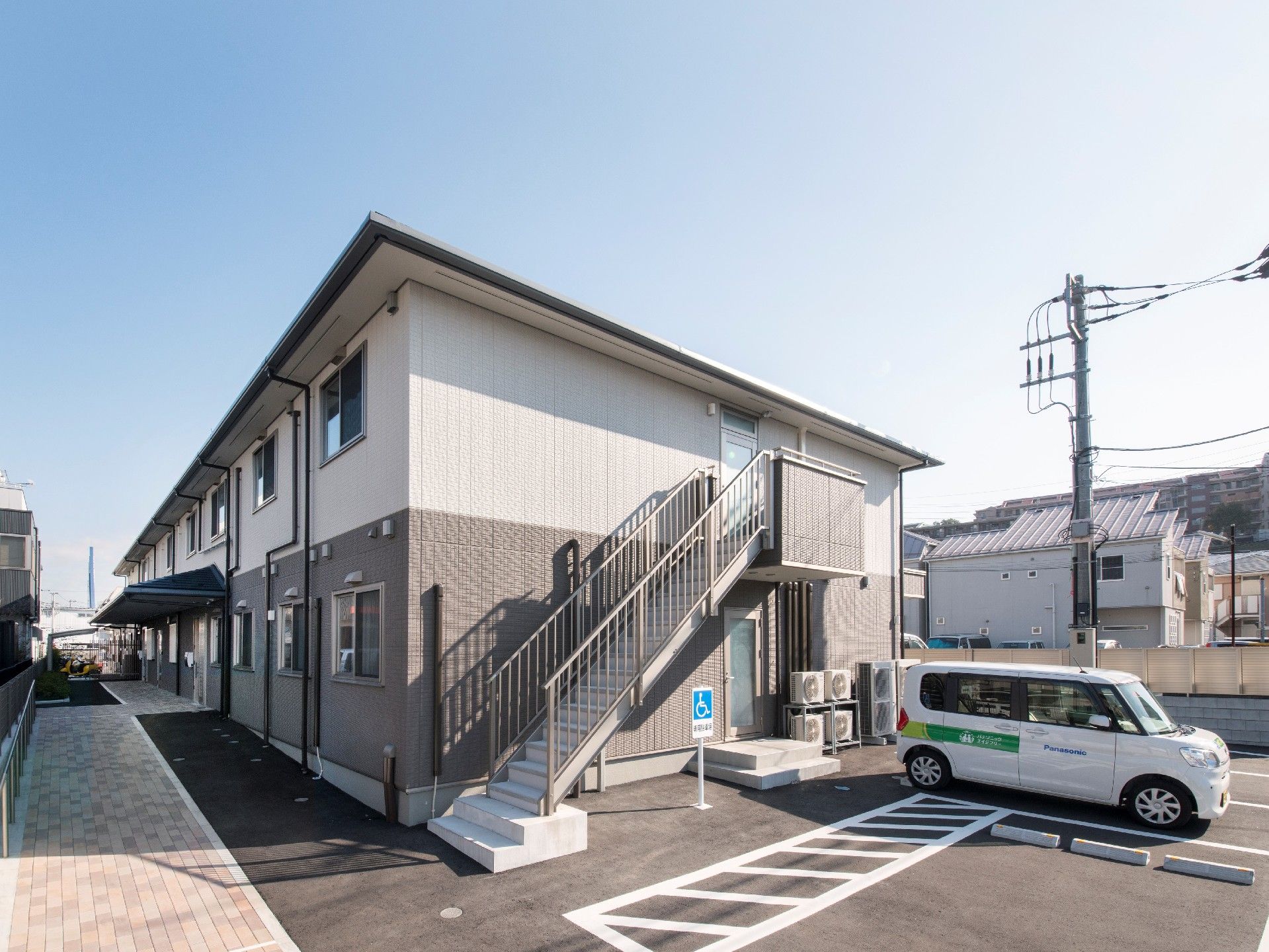 玄関に屋根が付いた2階建ての建物は白とグレーで、駐車場も完備されている。