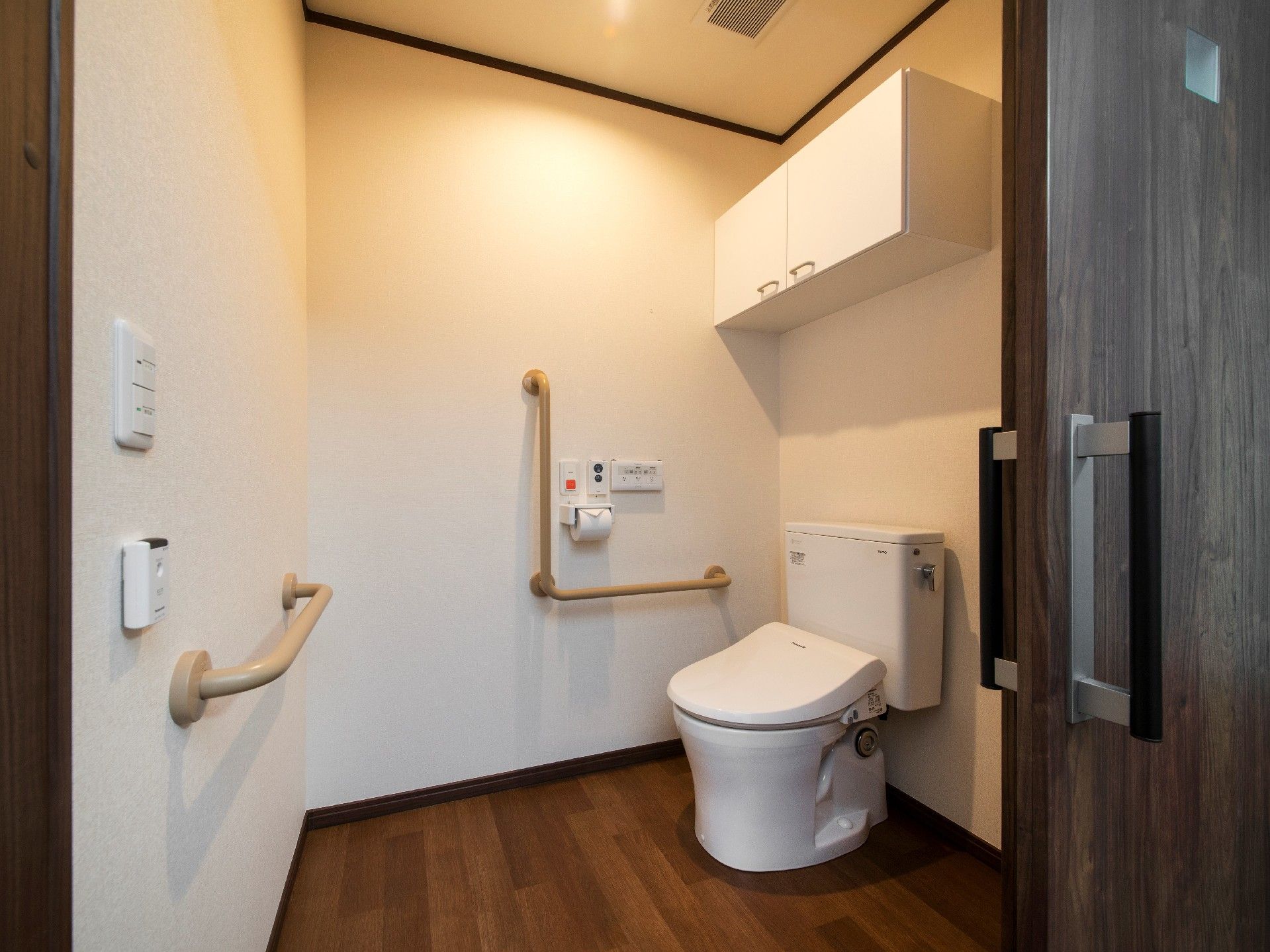 壁に収納や手すり、呼び出しボタンが付いたトイレは広く、フローリング。