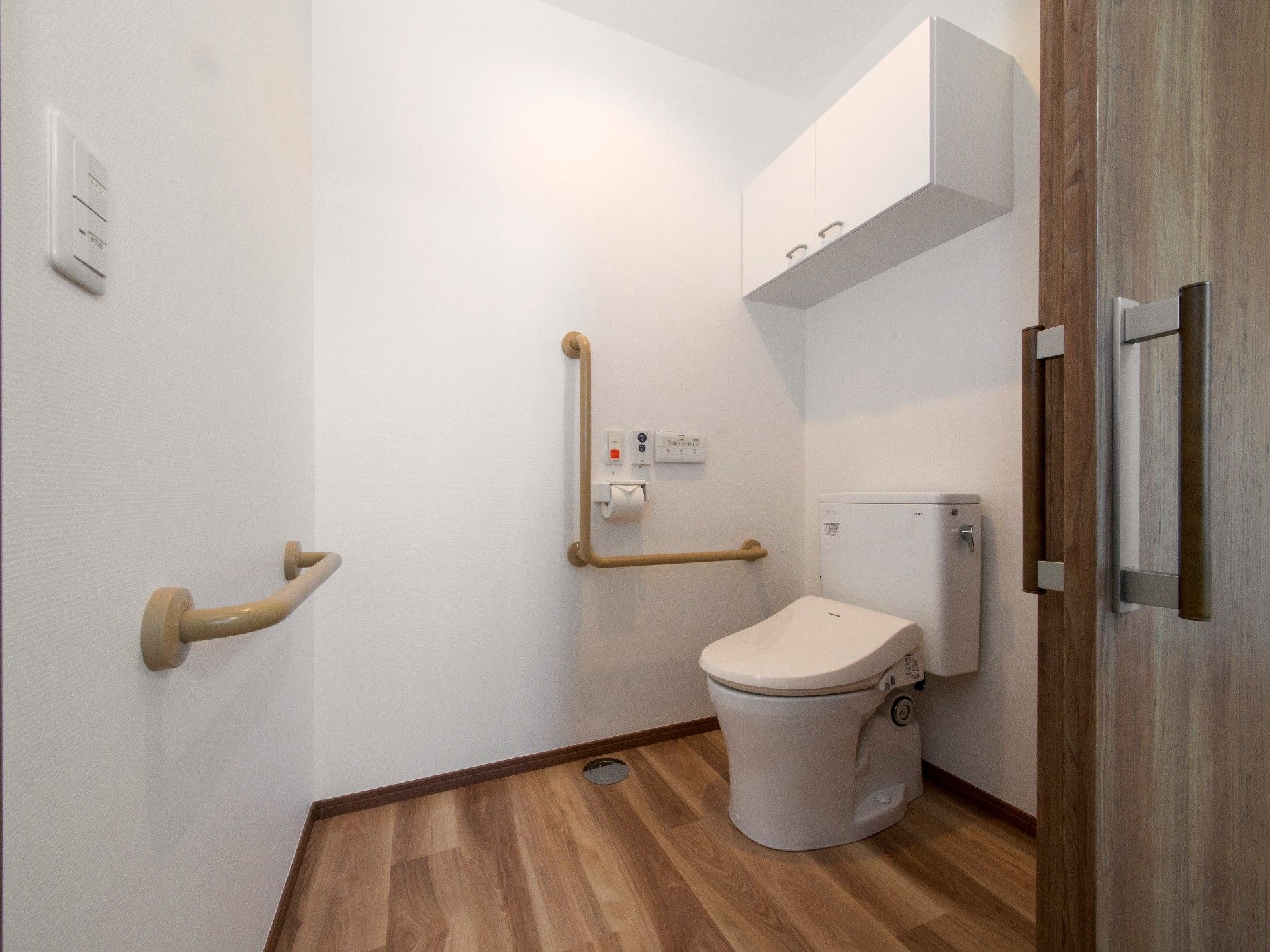 フローリングの床に白い壁。トイレにの横と前には手すりが付き、収納もある。