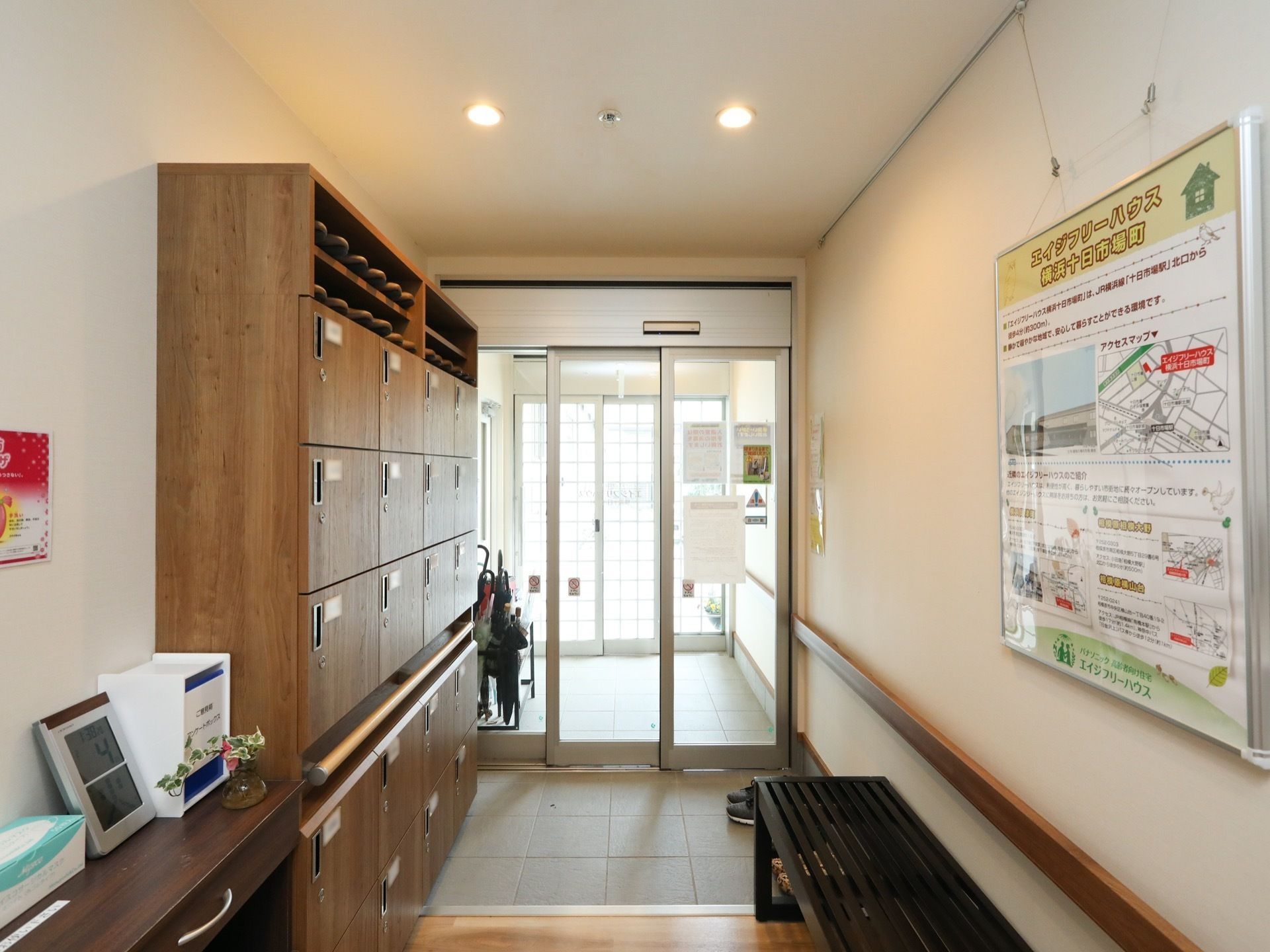 ガラス製の引違い扉の玄関である。壁際には、木製の大きな下駄箱収納が設置されており、天井にはダウンライトがある。