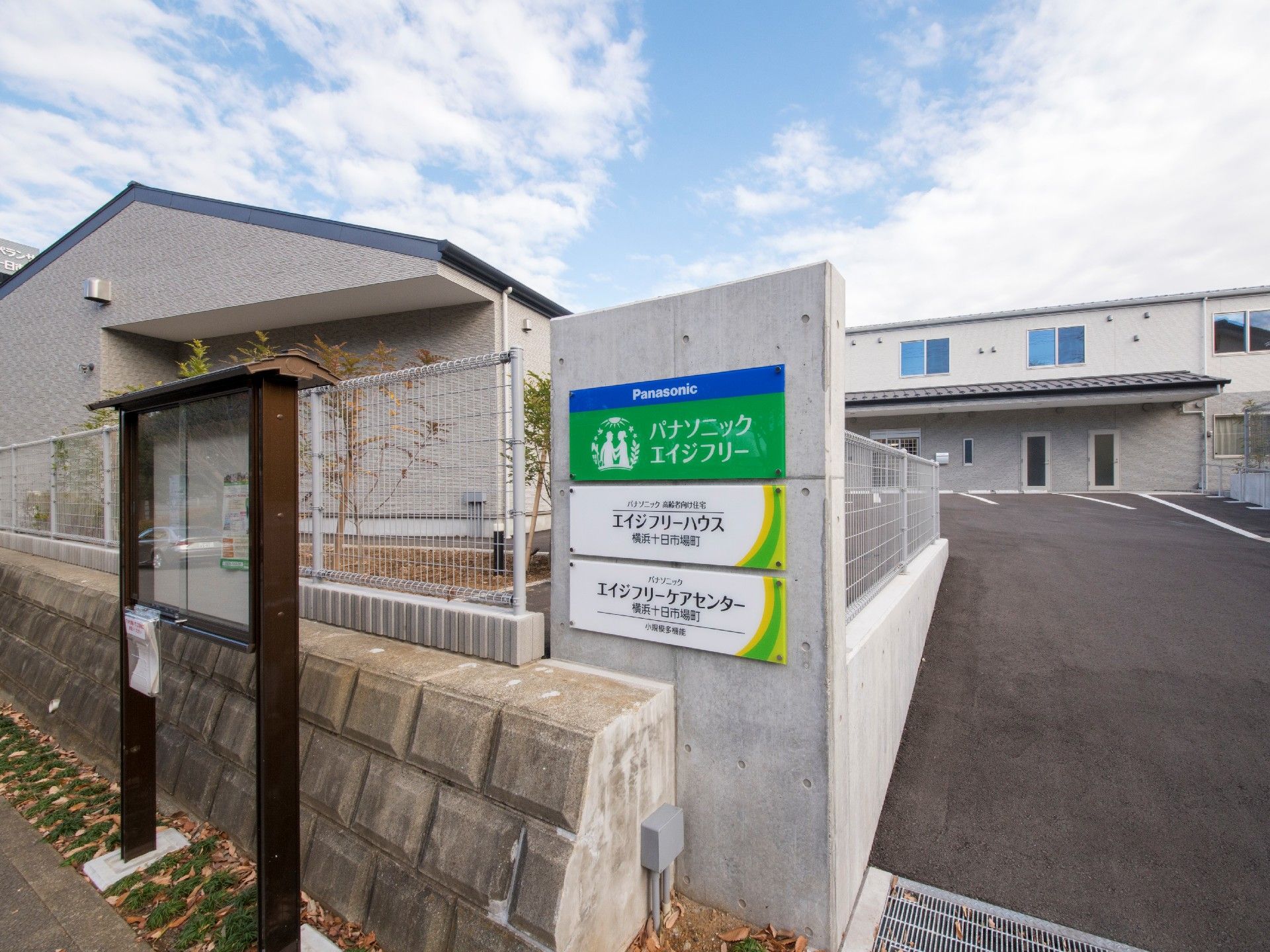 門の横には掲示板のようなものがあり、駐車場付きの敷地内には平屋建ての建物と2階建ての建物がある。