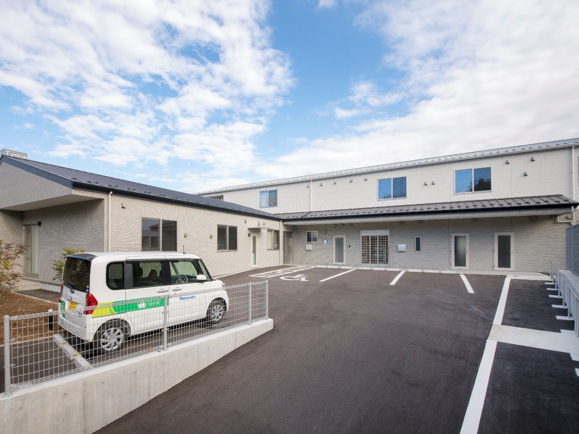 広い駐車場がある敷地内に、玄関に屋根が付いた２階建ての建物と平屋建ての建物がある。