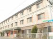３階建ての建物は明るいベージュっぽい色で、玄関の前には自動販売機がある。
