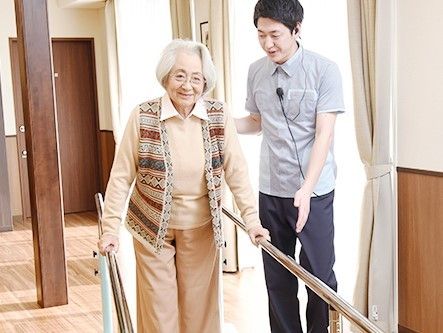 平行棒で歩行訓練をする女性入居者と、声かけをしながらついている男性スタッフ。