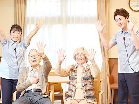 いすに座った男女の入居者とそのそばに立っている男女のスタッフが笑顔でレクリエーションに取り組む様子。
