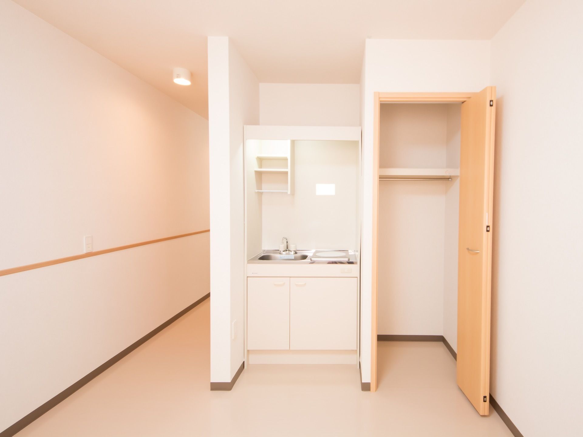 入居者様の居室にあるミニキッチン。流し台と電熱ヒーター、流しの上と下部分には収納スペースがある。隣の壁には大きなクローゼットがある。