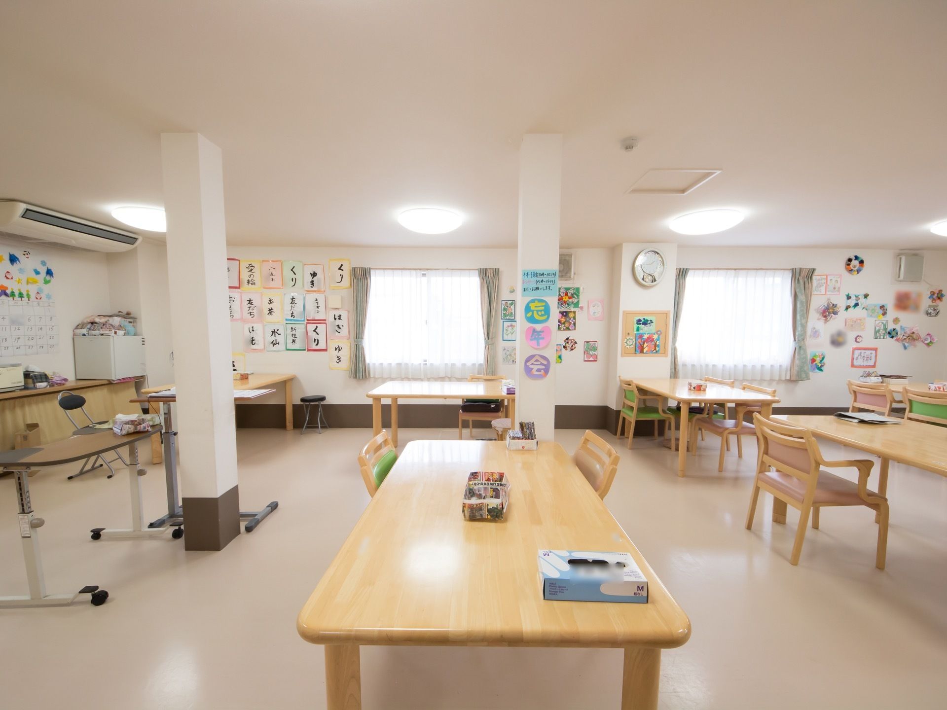 テーブルと椅子がたくさん並べられている広い食堂。真ん中に柱が立っている。窓が等間隔に配置され、壁には書道の作品や飾りつけがされている。