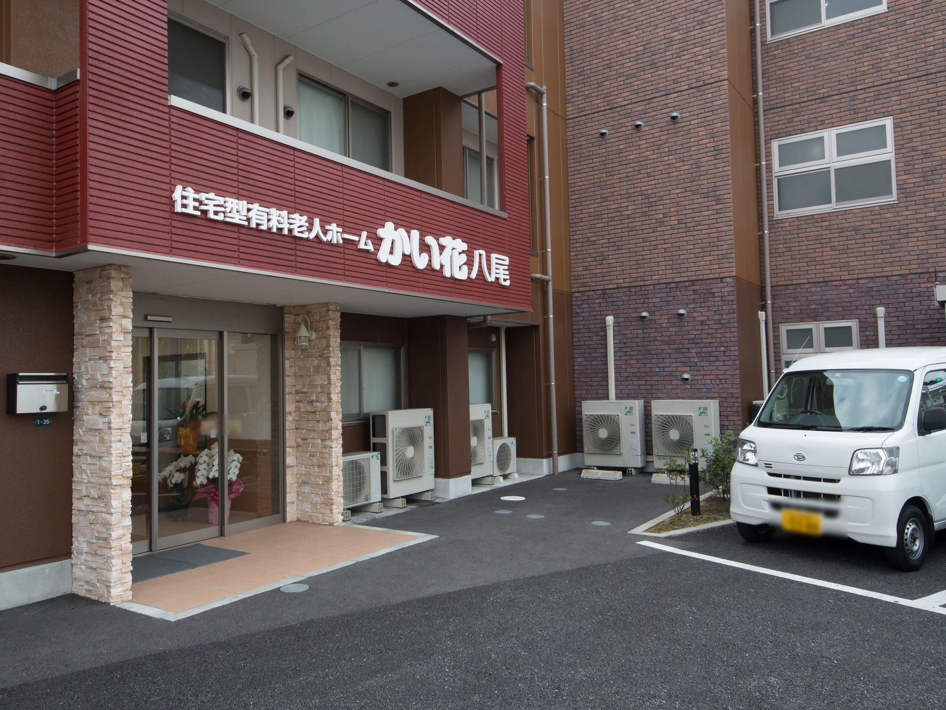 ブラウンを基調とした落ち着いた色合いの建物である。自動ドア近くの外壁には、ポストや照明が設置されている。