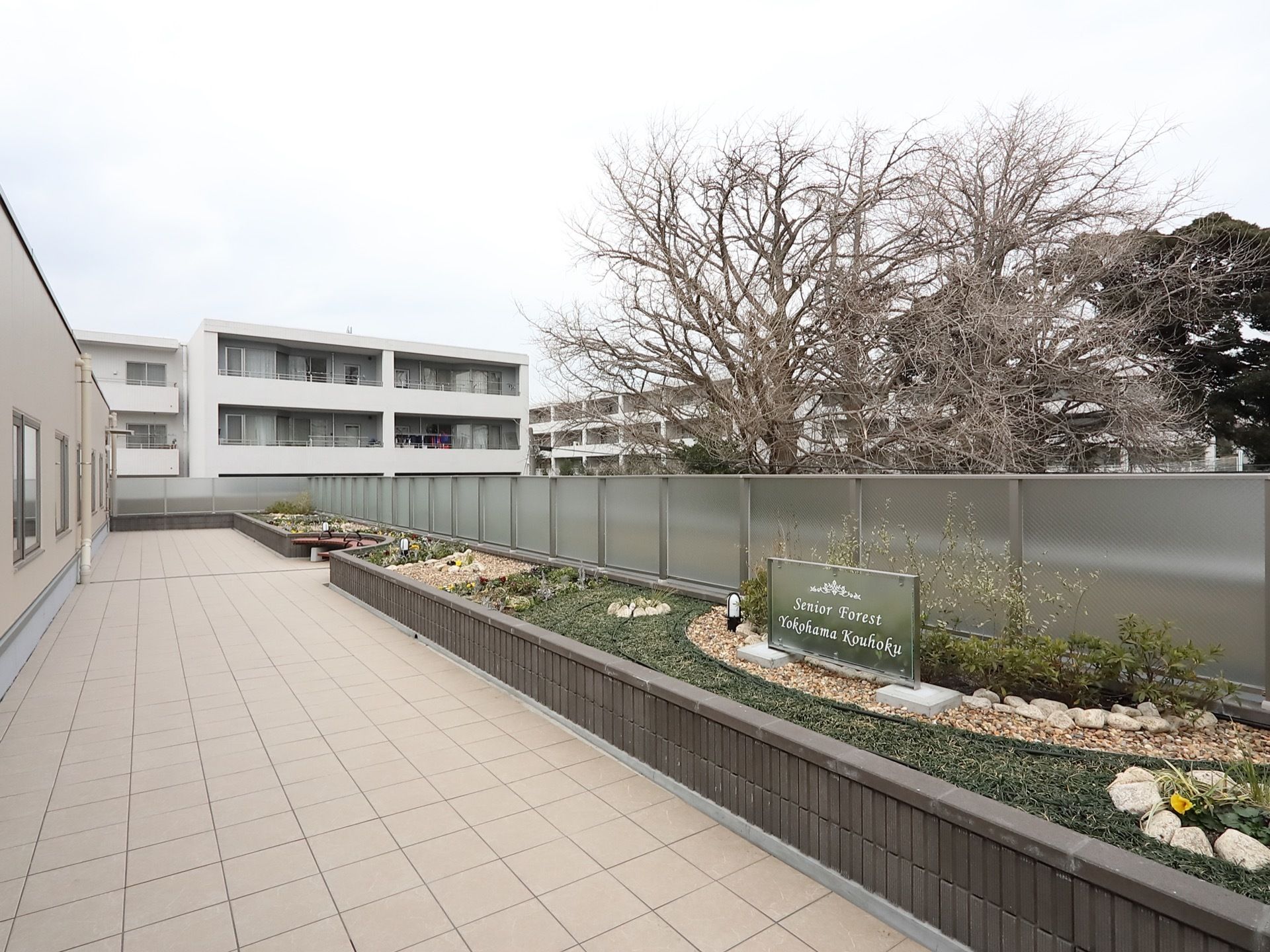 敷地内に共用のベランダがある。半透明のフェンスで仕切られ、その前に花壇がある。砂利などが敷かれ、花が植えられている。