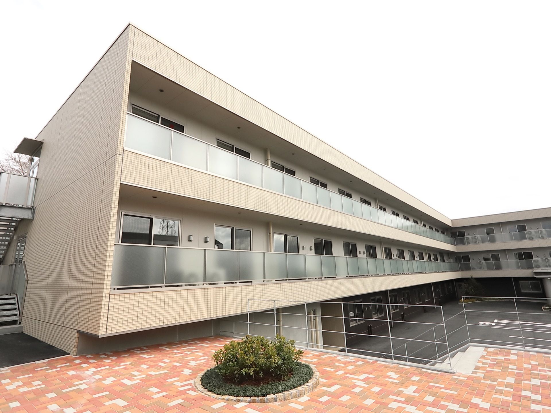 ３階建ての施設の建物のうち、２階以上の部屋には広いベランダが設けられている。非常用の外階段が見られる。