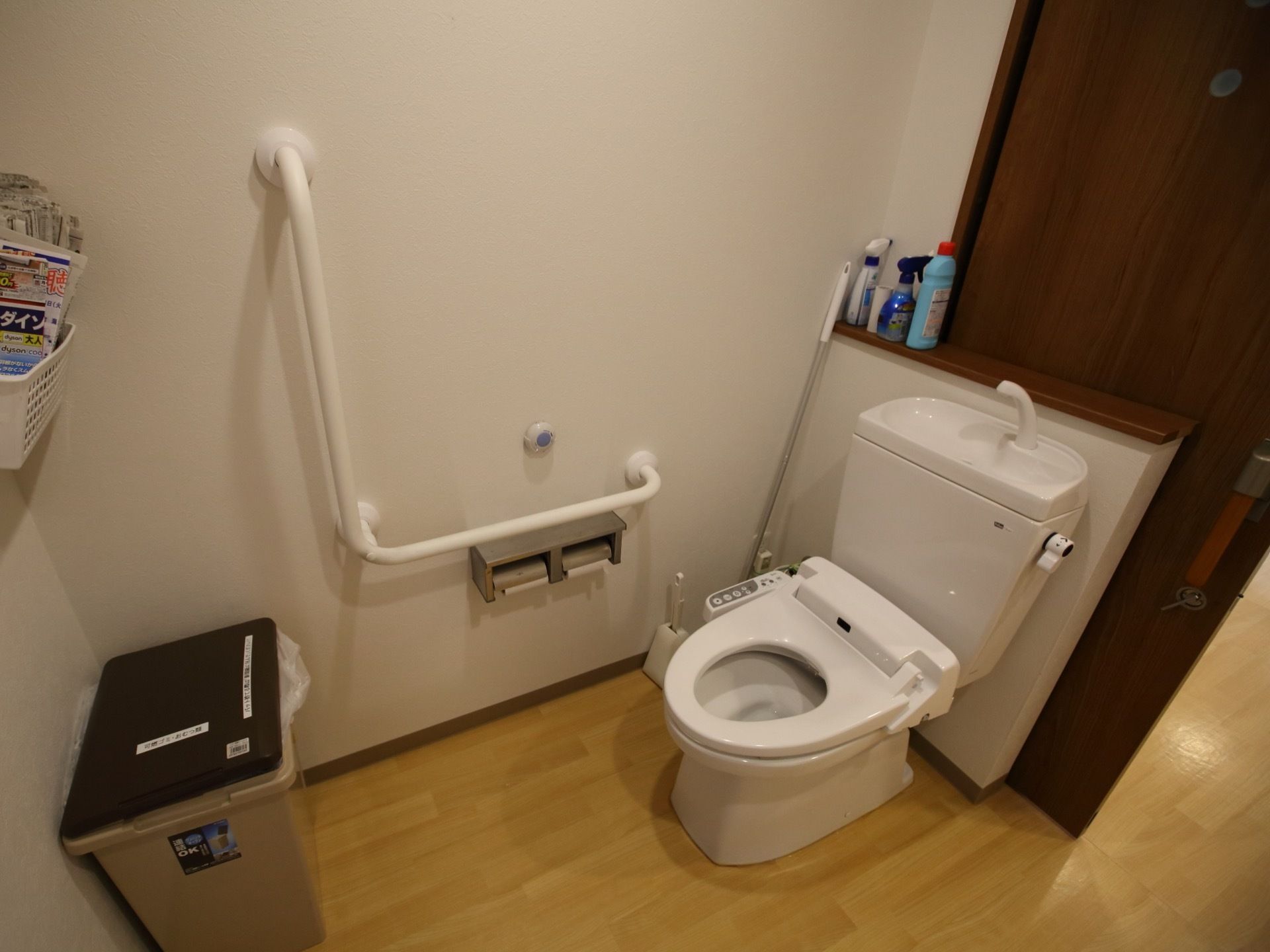 トイレは洗浄暖房機能つきの便座である。トイレットペーパーホルダーが２つ並んでいて、その上にL字型の大きな手すりがある。