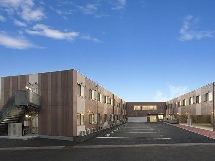 コの字型のブラウン系の建物の中央に駐車場がある。