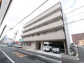 ５階建ての建物になっていて、２階以上にはベランダが付いている。１階の右側には車が２台駐車されており、建物の前には道路がある。