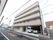 ５階建ての建物になっていて、２階以上にはベランダが付いている。１階の右側には車が２台駐車されており、建物の前には道路がある。
