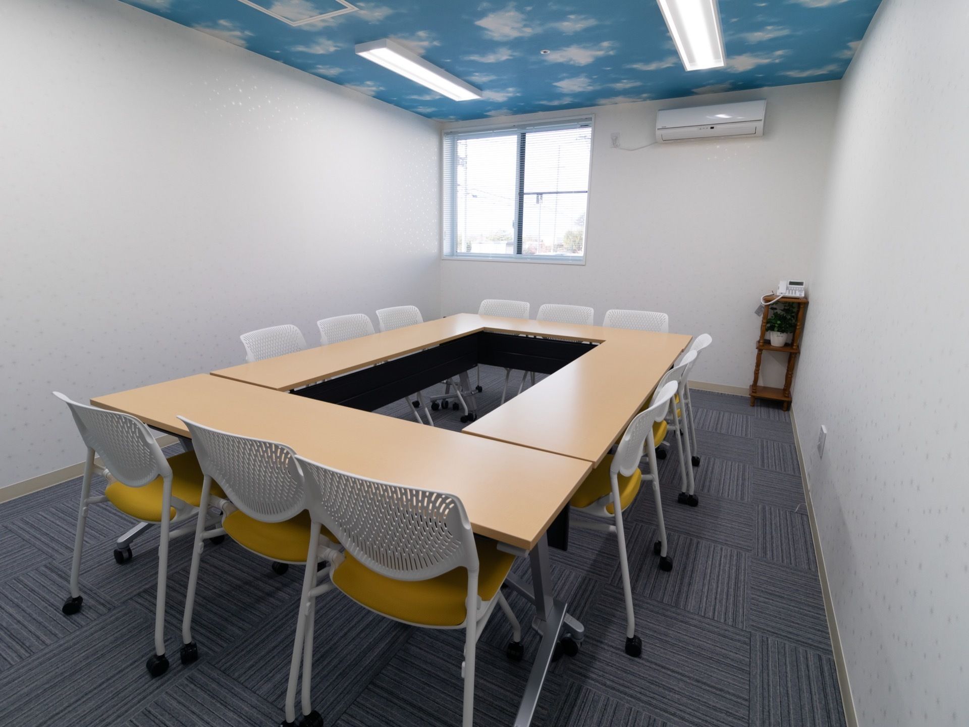 事務用品の机と椅子が並べられている会議室。部屋の角には内線対応の電話機、天井近くにはエアコンが取りつけてある。