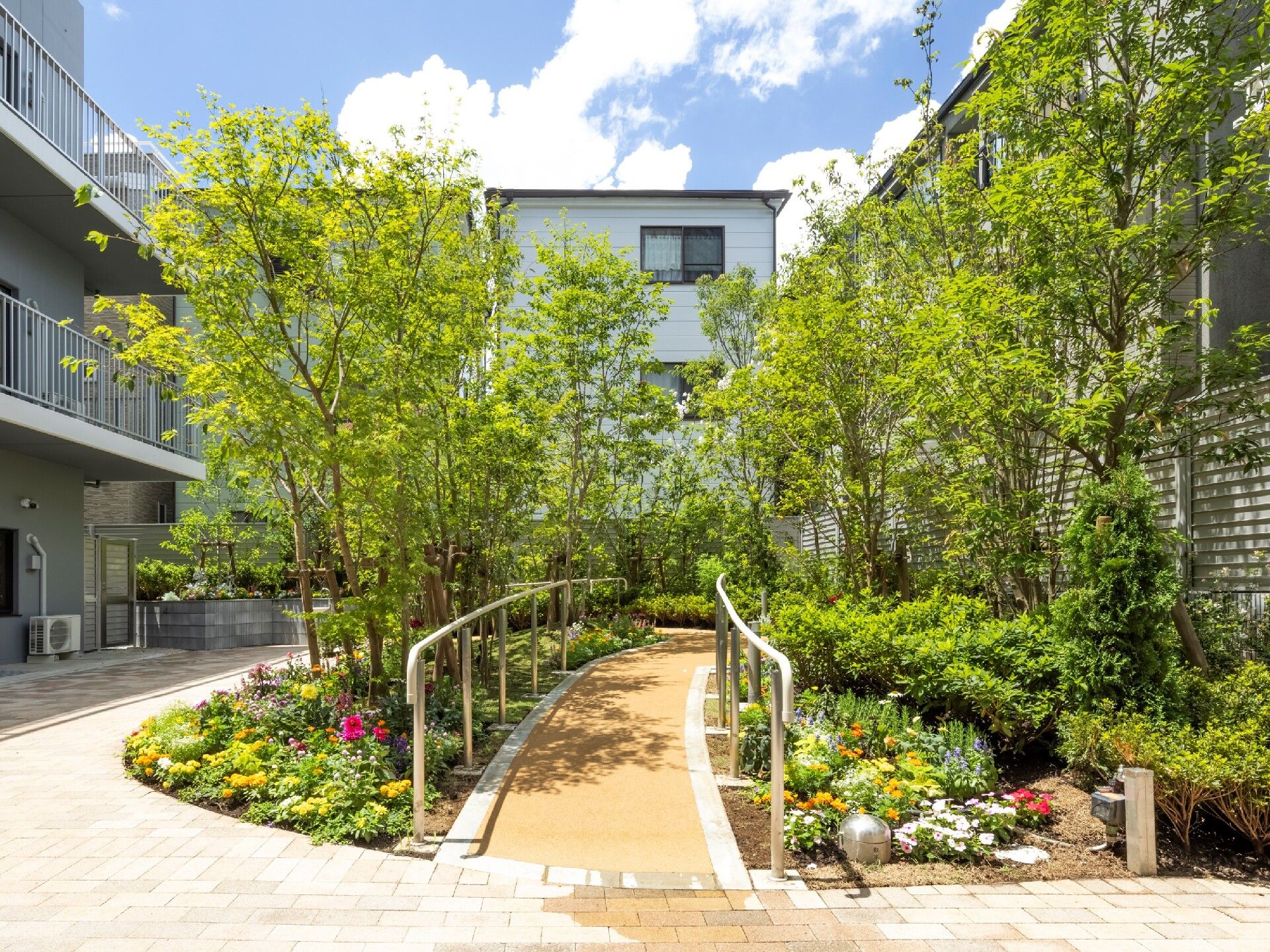 白や赤の花が植えられ、緑の木々に囲まれた遊歩道があり、手すりが付いている。庭を囲むように通路が続いている。