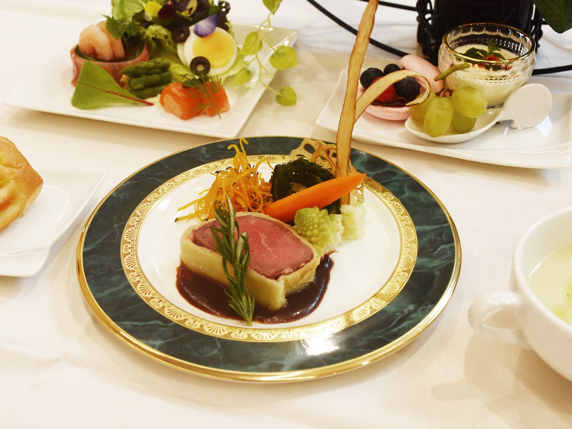 ローストビーフのパイ包みをメインとして野菜が添えられていて、スープやサラダ、前菜盛りなどが周りにある。