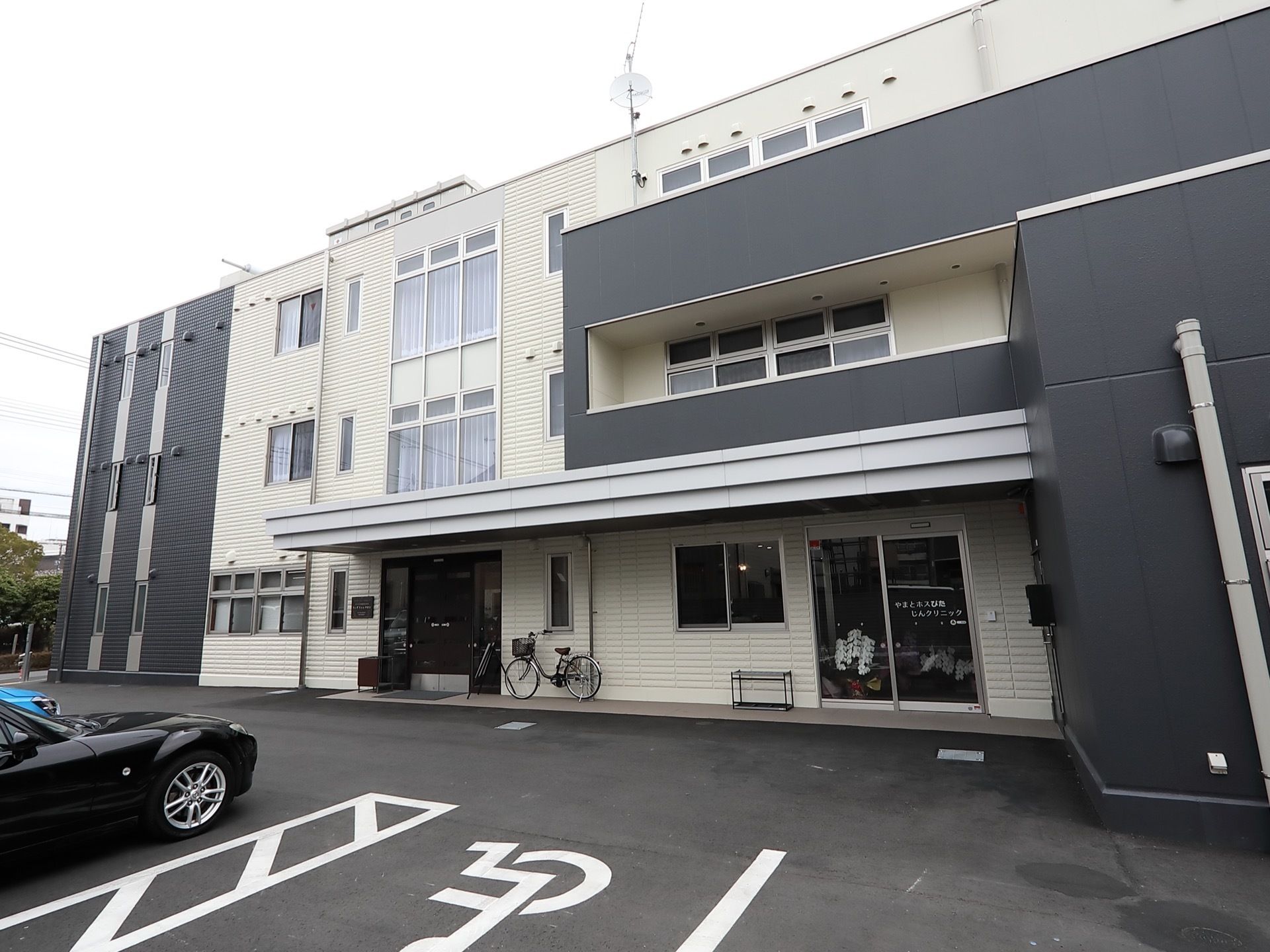 施設は、鉄骨３階建ての建物となっている。外壁は白と黒のツートンカラーでシンプルである。施設の前に駐車場が設置されている。