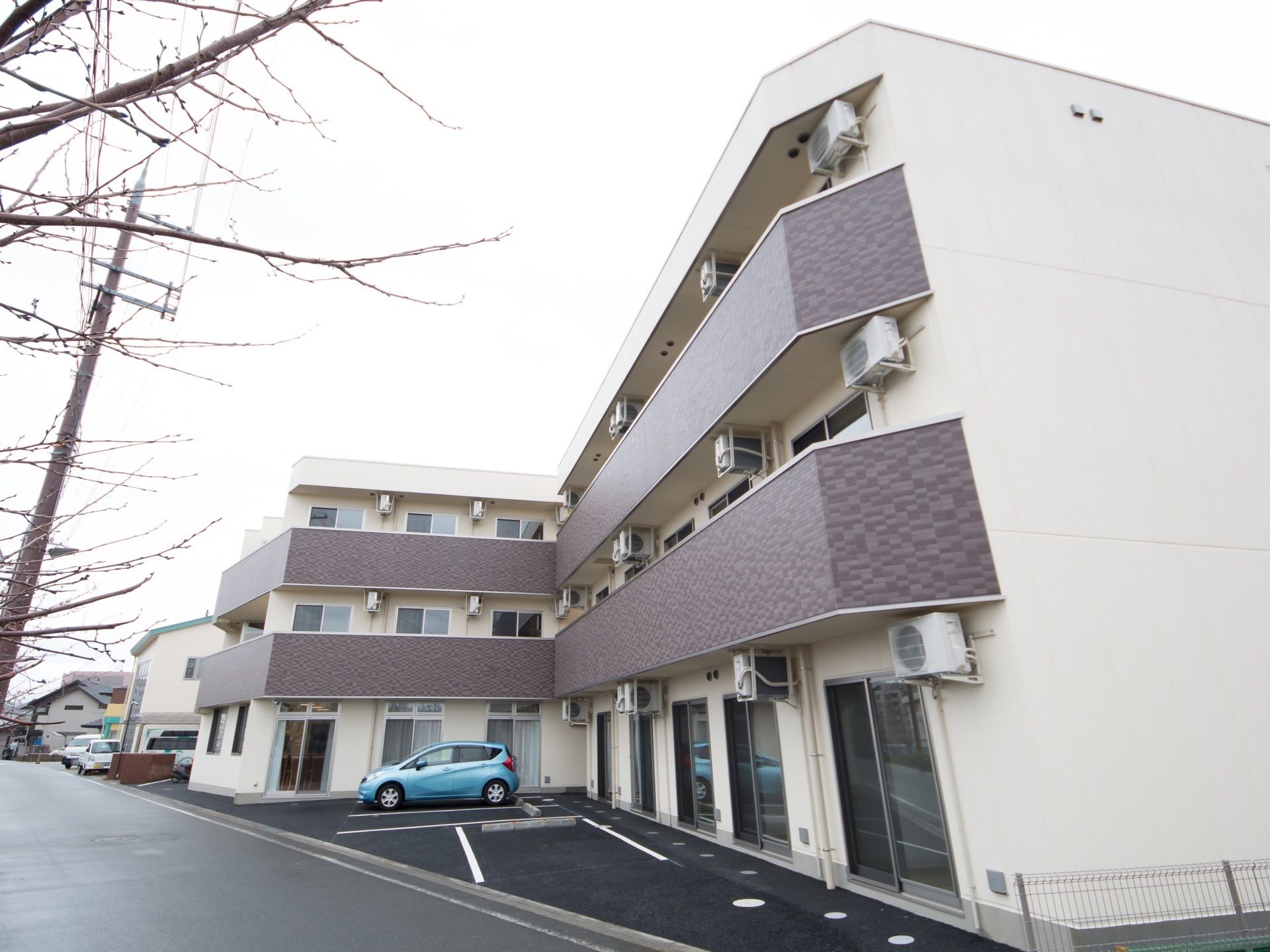 白をベースとした３階建ての施設外観である。２階より上の階の部屋には、掃き出し窓とバルコニーが設置されている。