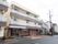 ３階建ての施設は、１階が濃いブラウン、上の階が白に塗り分けられている。玄関前にはスロープや花壇がある。