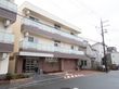 ３階建ての施設は、１階が濃いブラウン、上の階が白に塗り分けられている。玄関前にはスロープや花壇がある。