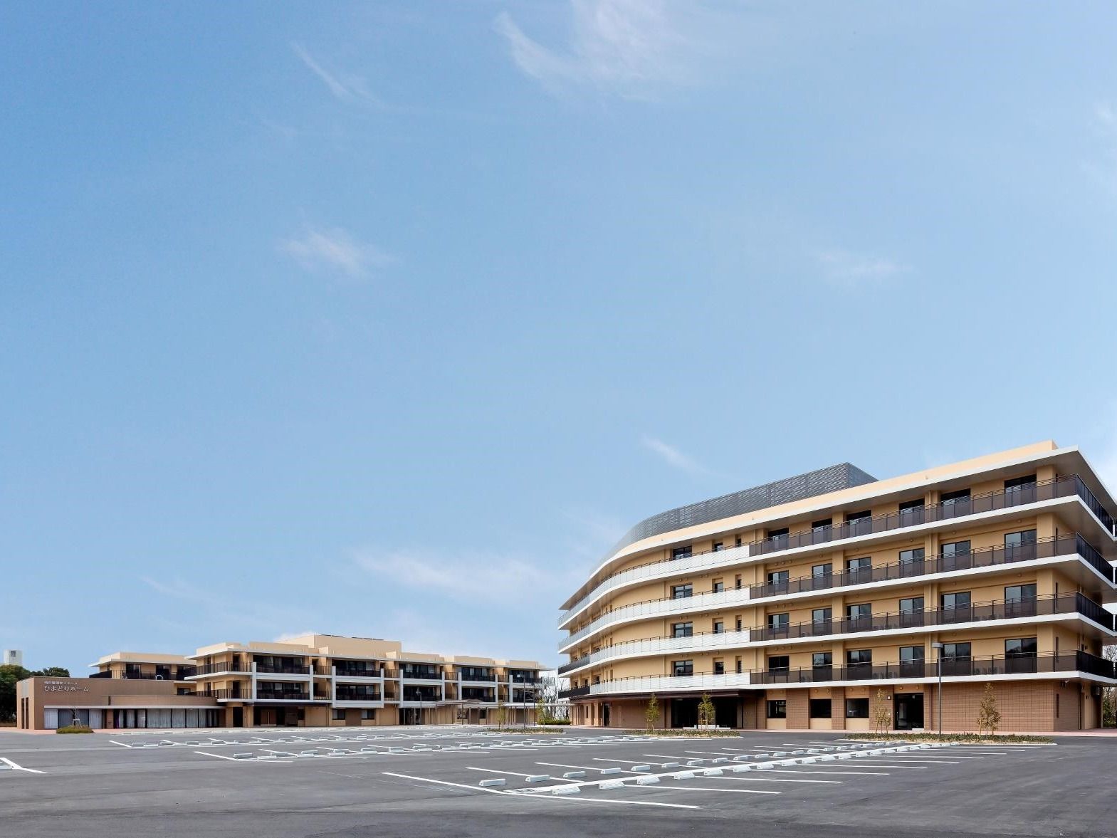 広い駐車場が付いた施設。手前には５階建ての建物、奥にはそれより低い建物がある。