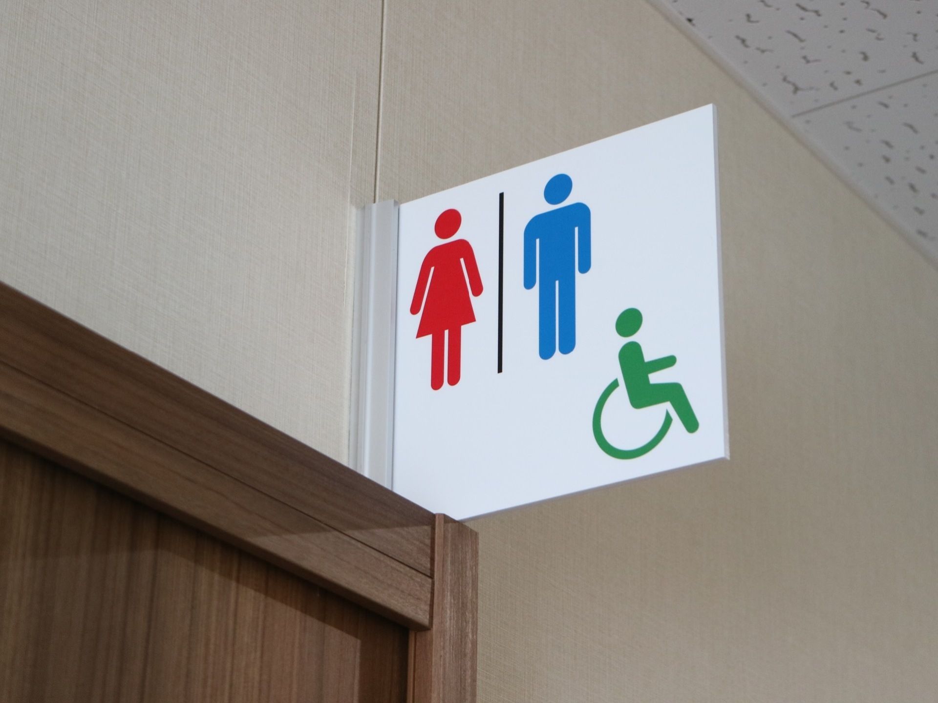 廊下の途中に、車椅子をご利用の方にも配慮された男女共用のトイレが設けられている。入口上部には、パネルが設置されている。
