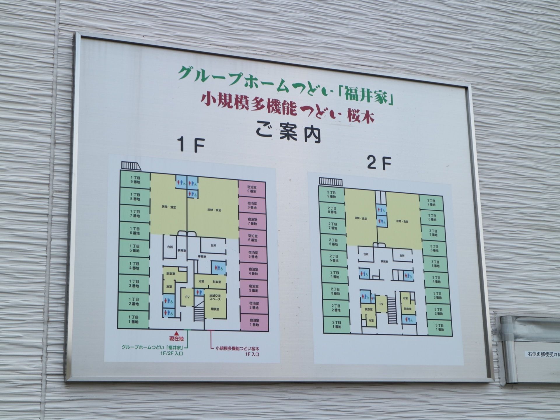 デザイン性のある壁に案内図が設置されており、１階と２階のフロアマップが表示されている。横には、郵便受けが設けられている。