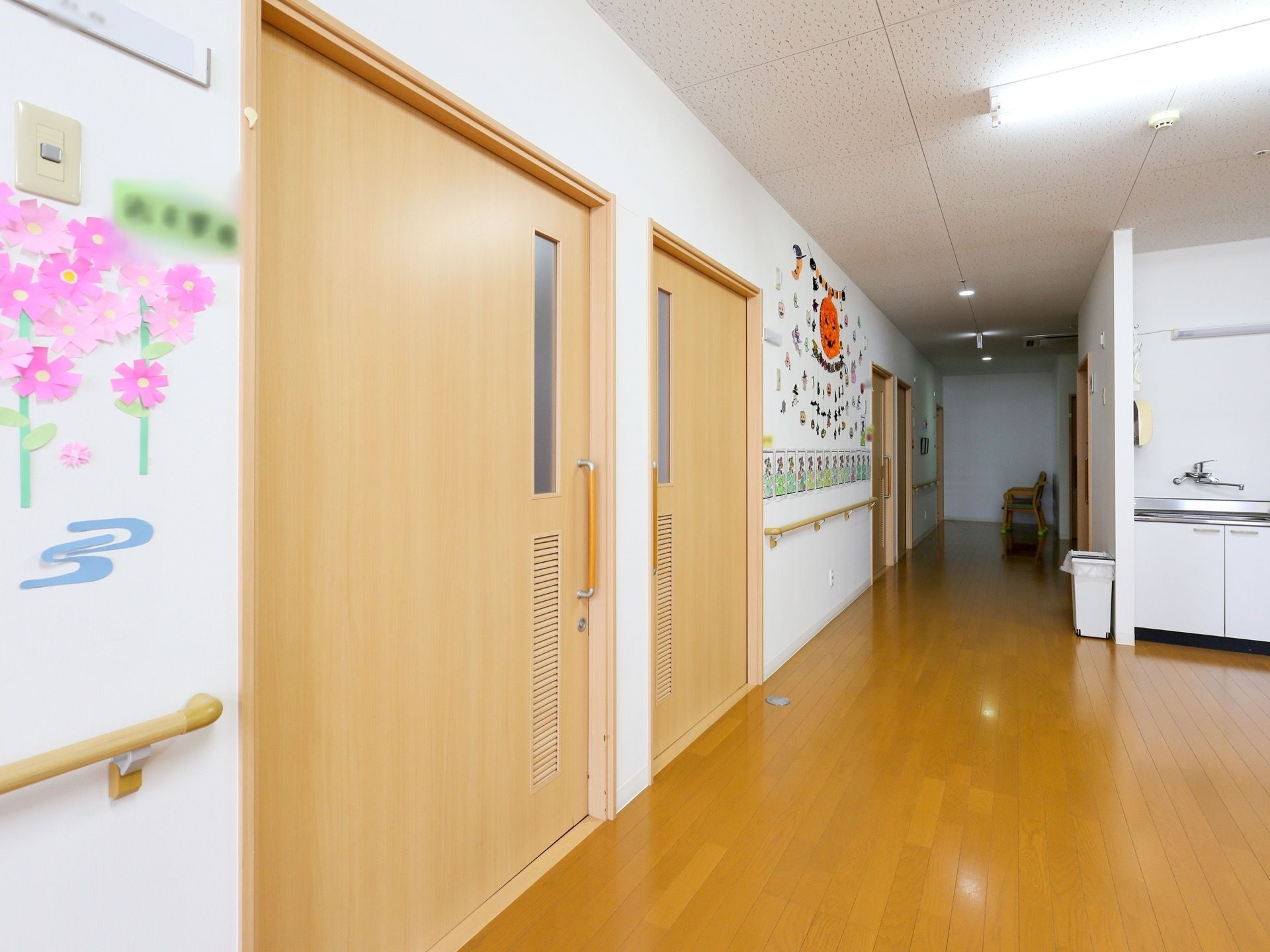 居室の扉が2つ並んでいる。扉横には入居者様の名前が書かれている。壁にはピンク色の花やハロウィンの飾り付けがされている。