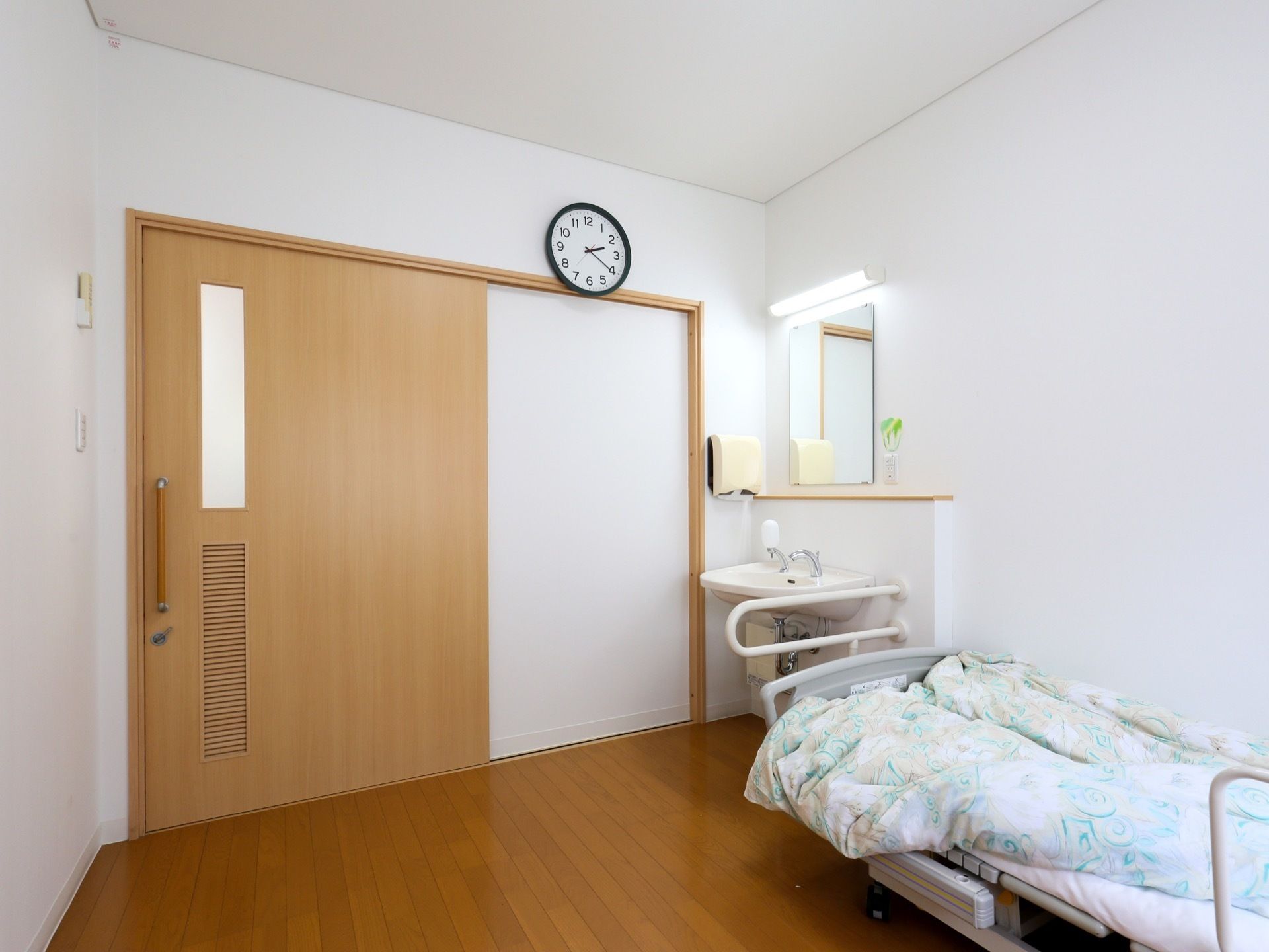 居室の扉は大きく、スライド式である。扉付近には洗面スペースやベッドが備えられている。壁には時計がかけられている。