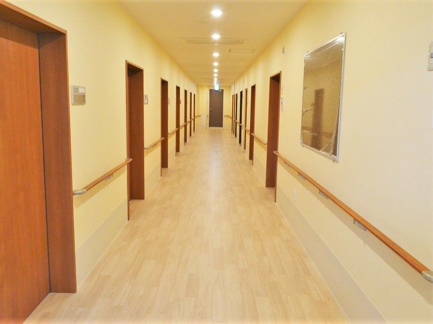 両サイドに居室があるまっすぐな廊下。手すりがあり、居室ドアは木製の引き戸。
