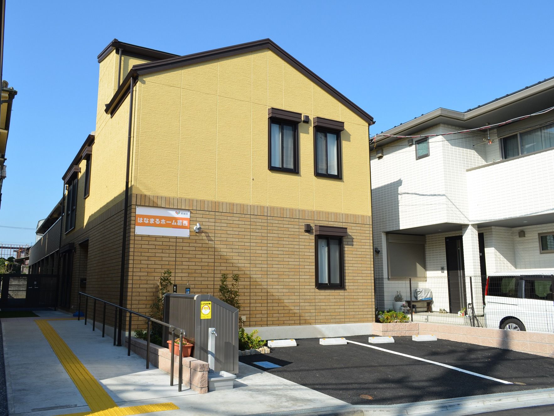 ２階建ての建物にはホームの看板が貼られている。上の階と下の階の色が異なるデザイン。