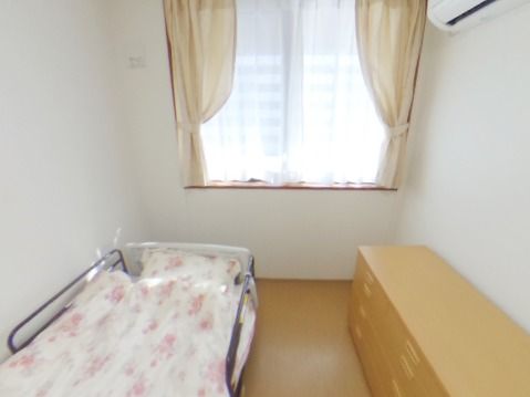 花柄のカバーがかかった布団が設置されたベッドやたんす、エアコンが設置された居室。