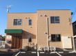 ブラウンの２階建ての建物。建物の玄関の周りには屋根が付き、日当たりもよい。