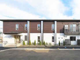 ブラウンと白の2階建ての建物は横に長く、駐車場も完備。建物の周辺には緑が多くある。