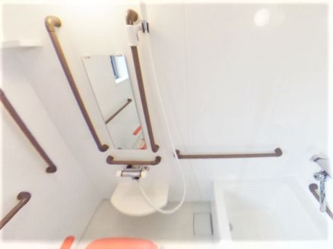 浴室は白い壁で茶色い手すり、シャワーも付き、シャワーチェアも置かれている。