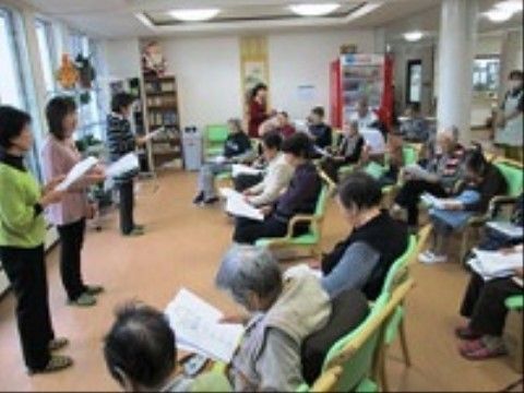 職員と入居者が歌詞カードを見ながら合唱を行っている