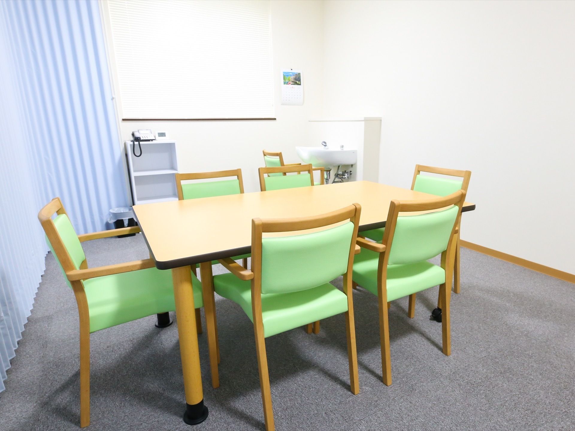 中央にあるテーブルを囲むように椅子が６脚置かれている。奥に洗面台があり、その手前にも椅子が用意されている。
