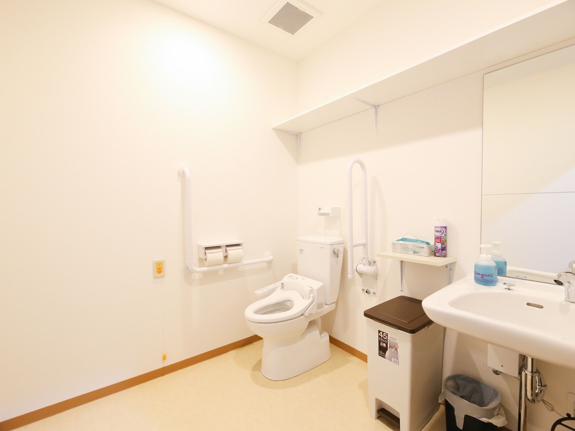 白い壁の広々とした個室トイレで、洋式便器が１つ設置されている。洗面台には大きな鏡が取り付けられている。
