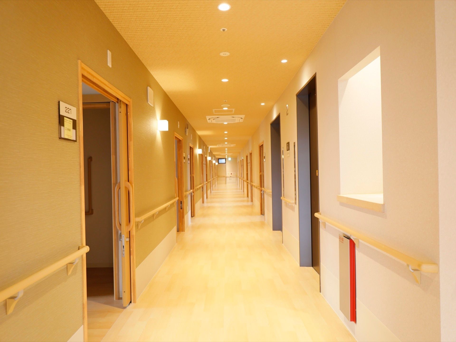 真っすぐ伸びた廊下で、両側に居室への引き戸が並んでいる。壁には部屋番号が書かれた表札が取り付けられている。