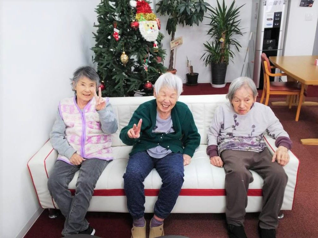クリスマスツリーが飾られた食堂の一角にあるソファに座って笑顔を浮かべる女性入居者3名。