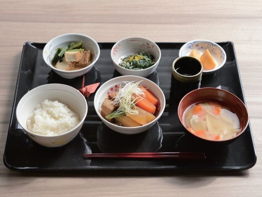 トレーに並べられた栄養バランスのいい食事。白いご飯にみそ汁、野菜の和え物、煮物などの和食。