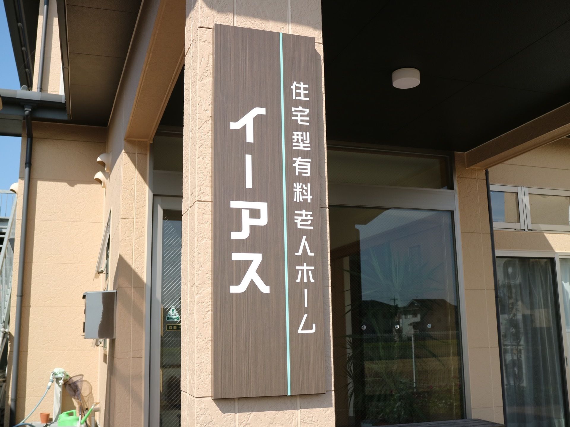 玄関前の柱に施設名の看板がある。屋根が取り付けられており、雨の日も濡れることなく出入りすることができる。