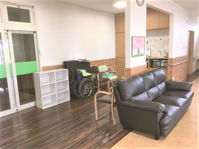 黒く大きなソファが置かれた教諭スペースにはいすや車いすが置かれ、奥にはまっすぐに廊下が続いている。
