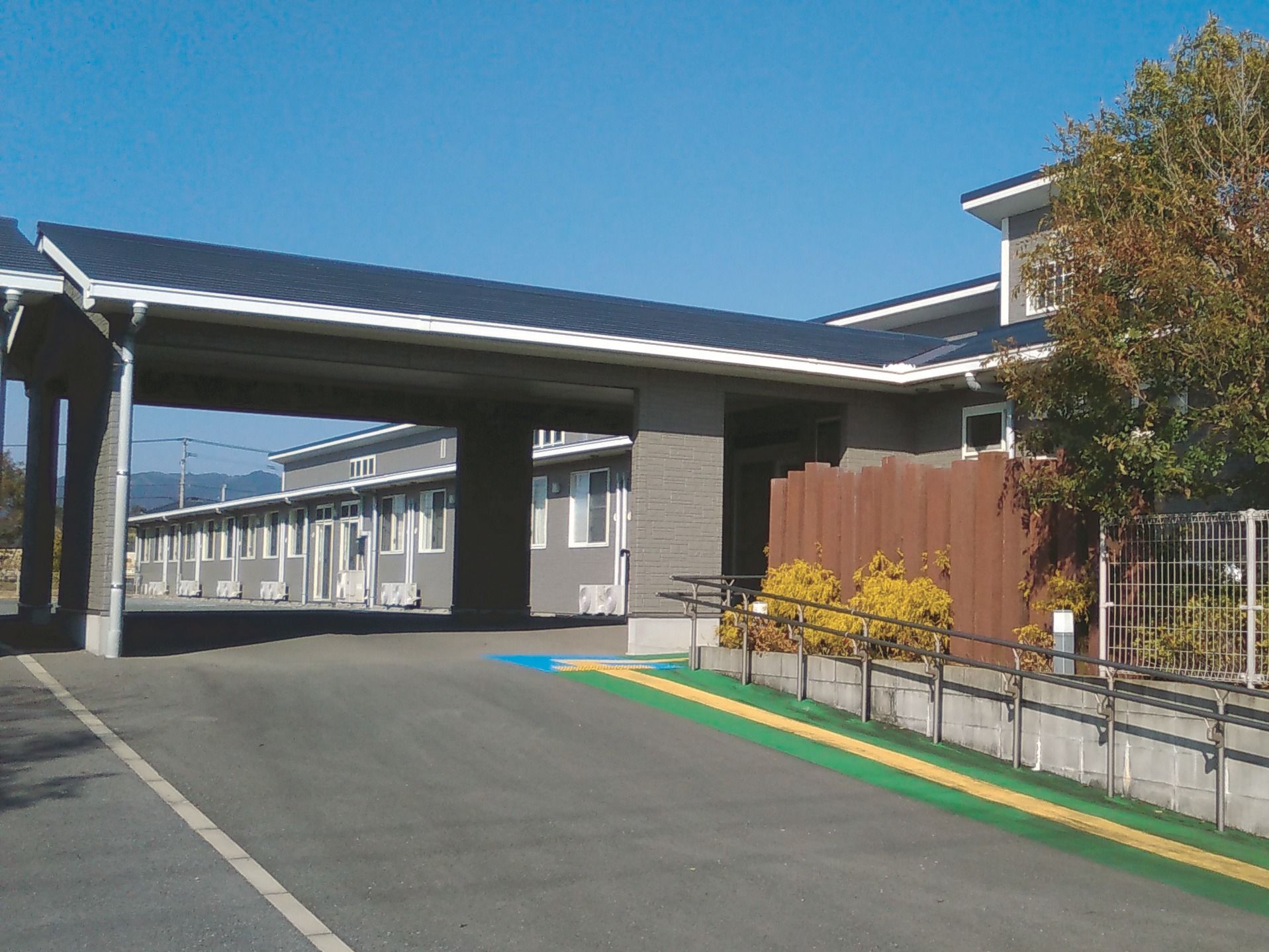 大きな車寄せが付けられたグレーの建物。ホーム周辺にはたくさんの木が植えられている。